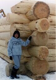 Linda Koski Standing next to Log Home