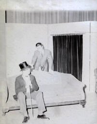 Masquers--"Enemy of the People" 1959: Man Sitting on Couch Wearing Top Hat with Another Man Behind Couch