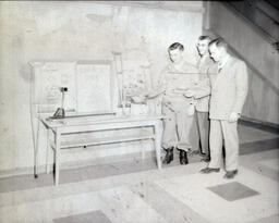 Charity Drive: Three Men Standing Next to "Drop a Dime" Campaign Table