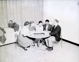 NMC International Club and Advisor Charles Mighell: Five People Sitting at Table Looking at Something on Table