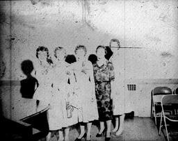 Rose Ceremony 1960: Five Women with Roses Stand by Piano