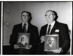 Two Men Holding Framed Pictures