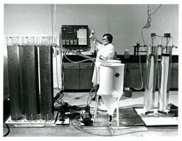 Woman Standing in Lab with Large Tubes of Liquid (Part of the NMU Historic Photographs Collection)