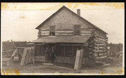 Two Men Leaning against Log Cabin