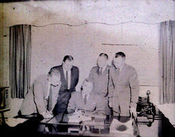 J. WIllis Owens, Kelli Mudd, and KI Sawyer Officials (Col. James W. Hold, Sgt. Emil E. Nond, Capt. John Hill): Four Men Leaning Over Man Sitting at a Desk