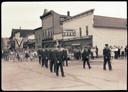 (050-021) Men In Uniform Marching Past Shamrock Bar in Ontonagon Labor Day Parade