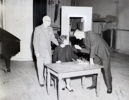 NMC Masquer's "The Night of January Sixteenth": Woman at Desk on Stage with Two Men