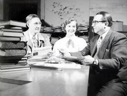 Faculty: Two Men, One Woman Seated With Books