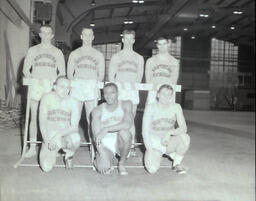 NMC Track Team 1961: Seven Track Athletes Surrounding Hurdle