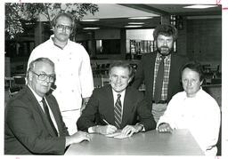 Group Shot of Men with Man Writing Check (Part of the NMU Historic Photographs Collection)