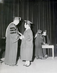 Commencement--Dr. Harden and Corlinne Truitt Jan. 1961: Woman in Graduation Gown Receiving Diploma and Shaking Hands with Man on Stage